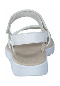 White sandal with a textured upper, adjustable ankle strap, and a cushioned light beige footbed. Features a thick white sole.