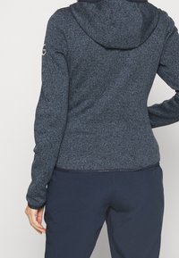 Marinblå hoodie i strukturerad tyg med dragsko i huvan och logotypdetalj på ärmen, kombinerad med marinblå byxor.