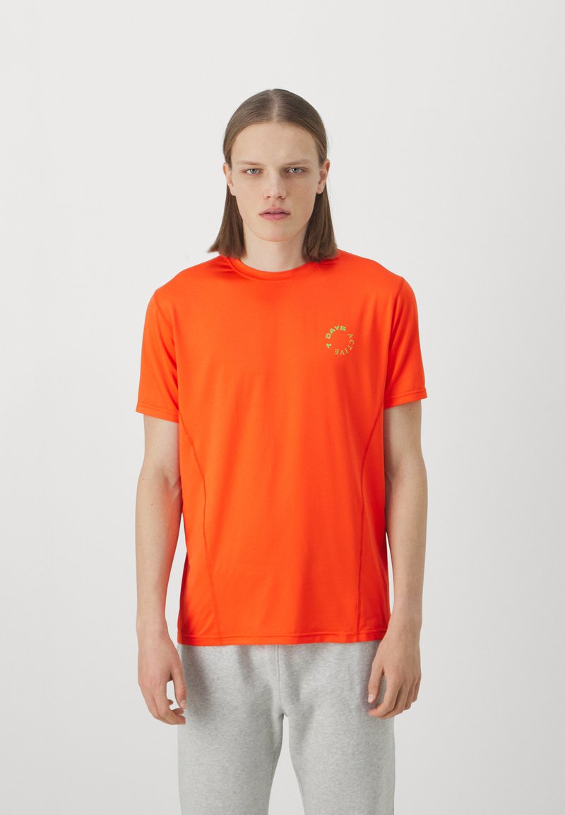 Lyst orange kortærmet trænings T-shirt lavet af glat, letvægtsstof med et grønt logo på venstre bryst. Simpelt, tætsiddende design.