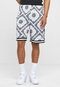 Black and white patterned shorts with a bandana design, elastic waistband, and black trim at the hem, paired with white sneakers and socks.