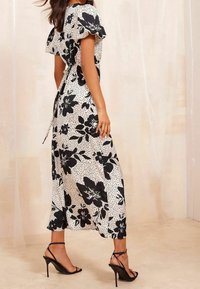 Maxi šaty s černobílým květinovým potiskem a tečkovaným vzorem; mají krátké volánkové rukávy a zavazování v pase. Černé sandály na podpatku.