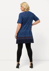 Robe courte à manches courtes bleue à motifs floraux avec un ourlet à motifs, associée à des leggings noirs et des chaussures à talons. Texture de tissu lisse.