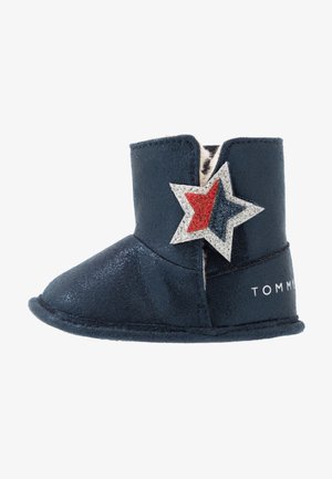 Navyblå babystøvle med blød sål, hvid pelsforet, et rødt og blåt glitrestjernebadge og "Tommy" branding på hælen.