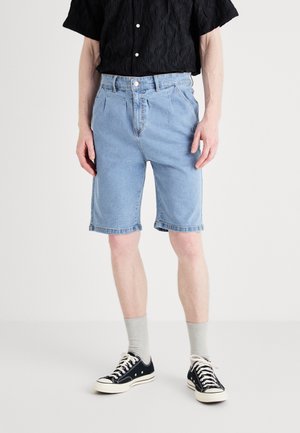 Svetlo modré denimové šortky s voľným strihom, so zošitými manžetami a klasickým dizajnom s piatimi vreckami. V kombinácii s čiernou štruktúrovanou košou a teniskami.