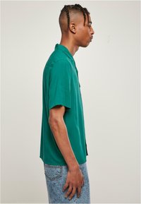 Korte mouwen, groen shirt gemaakt van gladde stof, met een kraag en een rechte snit. Gemaakt met lichtblauwe, verwerkte denim shorts.