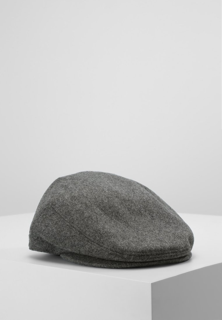 Casquette plate grise en tissu de laine reposant sur une surface blanche devant un fond uni gris clair.