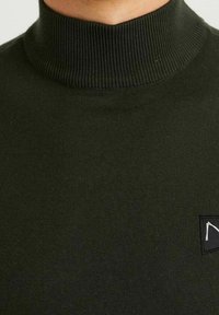 Musta ribatutrikoo, tummanvihreä pipo, jossa on pieni musta logopatch vasemmalla rinnan puolella.