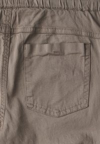 Tissu en coton marron avec une texture lisse, comportant une poche arrière rectangulaire discrète et des surpiqûres le long des coutures.