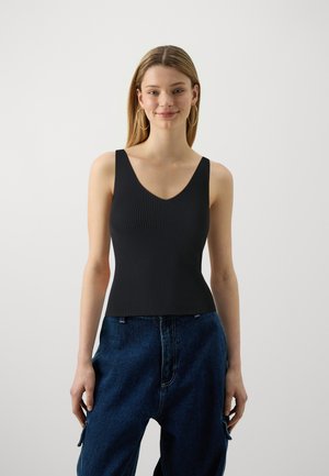 Black ribbed tank top with a deep V-neck and wide straps, fitted design, paired with loose blue denim pants. Simple, textured fabric.