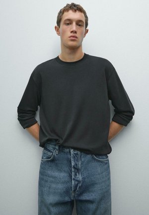 Sort langærmet skjorte med rund halsudskæring, parret med lyseblå denim jeans. Skjorten har oprullede manchetter og en afslappet pasform.