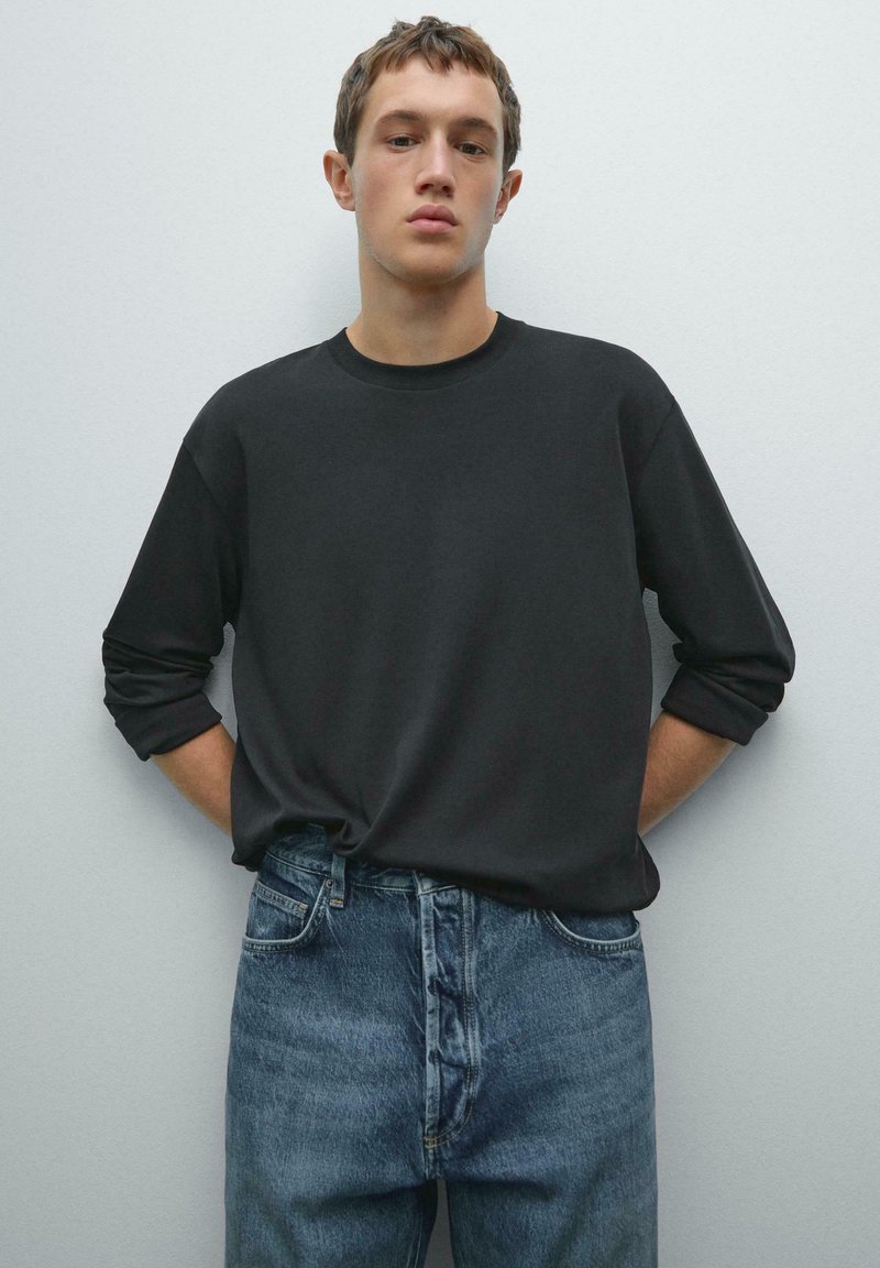 Sort langærmet skjorte med rund halsudskæring, parret med lyseblå denim jeans. Skjorten har oprullede manchetter og en afslappet pasform.
