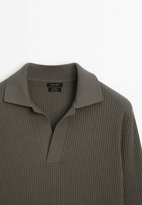 Oliven grøn ribbestrikket pullover med en splitkrave, der har et struktureret stof og et lille logo-tag nær halsudskæringen.