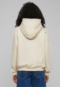 Kremfarget hettegenser med avslappet passform, med nedfellede skuldre og ribbestrikkede mansjetter, kombinert med blå denimjeans.