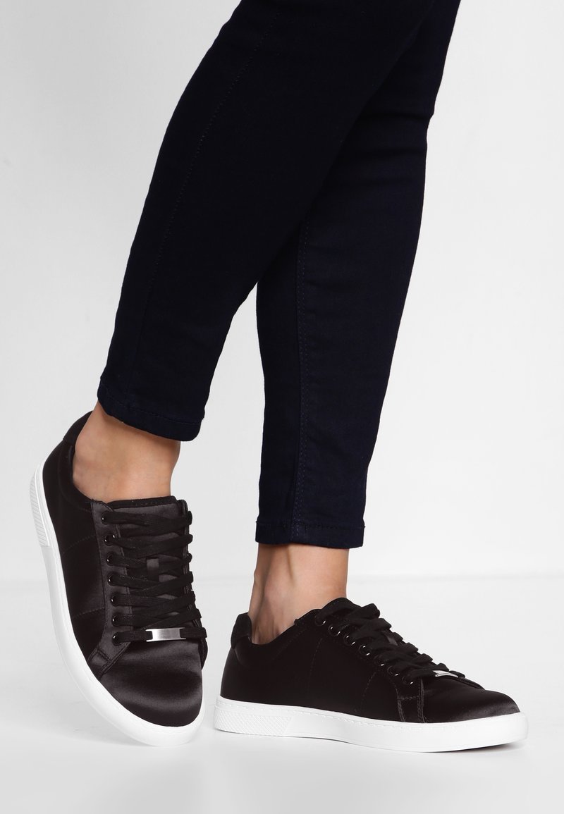 Baskets basses en satin noir avec semelles en caoutchouc blanches. Caractérisées par un design à lacets, des surfaces texturées et un petit accent métallique à l'avant.