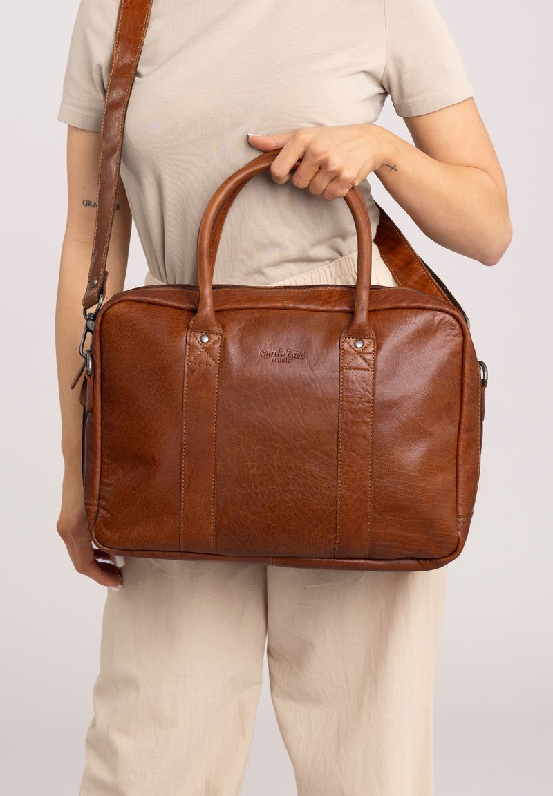 Brown leather bag with twin handles and detachable shoulder strap; features a smooth texture and visible stitching accents.