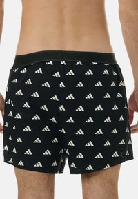 Svarta badshorts med ett vitt triangulärt mönster, elastisk midja och avslappnad passform, lämpliga för vattenaktiviteter.