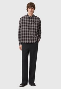 Camicia a quadri bianca e nera con colletto a bottoni, maniche lunghe e vestibilità rilassata, abbinata a pantaloni neri e scarpe nere.