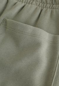 Joggers in cotone verde chiaro con vita elastica e tasca laterale. Texture liscia con un dettaglio di cucitura nascosta sulla tasca.