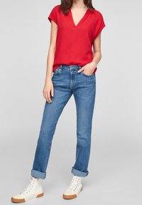 Rød top med korte ærmer og V-hals, kombineret med lyseblå jeans med lige ben og hvide høje sneakers med gummisåler.