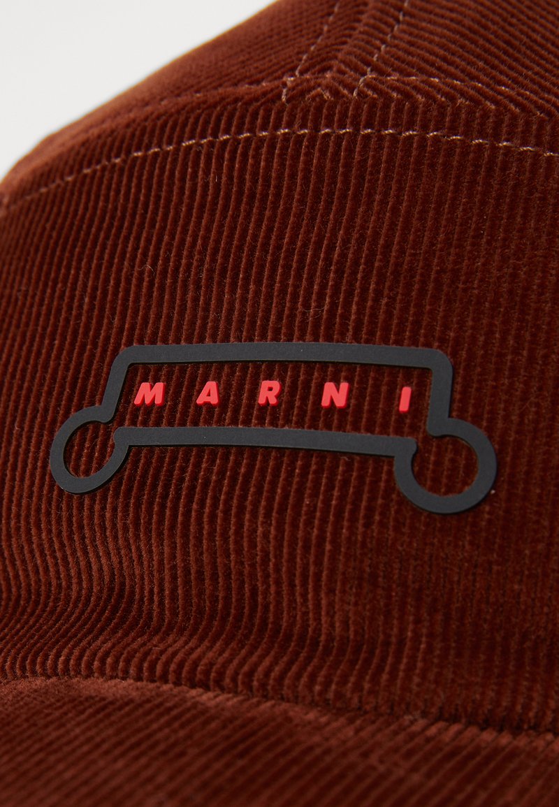 Brown corduroy cap featuring a black rubber logo with red text "MARNI." Texture shows vertical ridges; cap shape is classic with a stiff front.