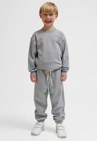 Grauer Pullover mit Rundhalsausschnitt, passende graue Sweatpants mit elastischem Taillenbund und Kordelzug sowie weiße Turnschuhe.