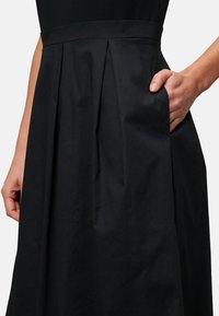 Black pleated skirt featuring a side pocket, made of smooth fabric with a structured waistband and a clean silhouette.