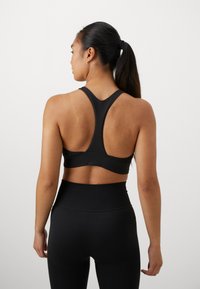 Svart treningstop med racerback-design, glatt tekstur og tettsittende stil, kombinert med høyhalsede svarte leggings.