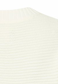 Close-up af en hvid strikket sweater med ribdet hals og tekstureret mønster i hele stoffet.