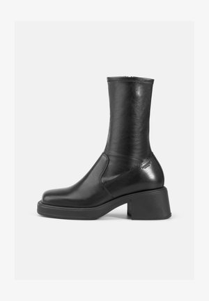 Zwarte leren enkelboot met een gladde afwerking, vierkante neus en een chunky blokhak. Bevat zijnaadstiksel en een subtiele metalen accenten.