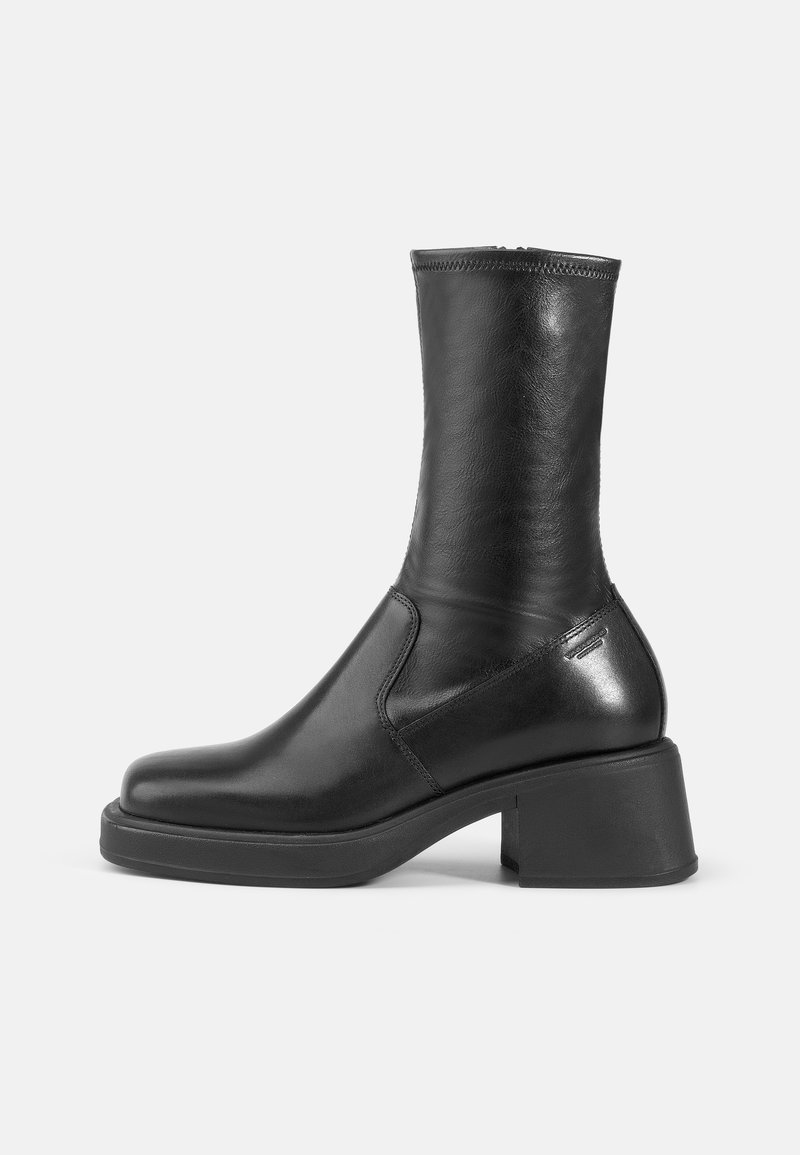 Bottine en cuir noir avec une finition lisse, bout carré et un talon bloc épais. Présente des coutures latérales et un subtil accent métallique.