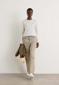 Camicia a maniche lunghe a righe in crema e blu navy, pantaloni beige a gamba larga, sneakers bianche, che porta una giacca marrone e un cappello beige. Design minimalista.