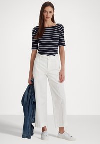 Haut marinière bleu marine et blanc à col bateau, pantalon large blanc, veste en jean et baskets blanches. Ceinture avec une boucle ronde en argent.