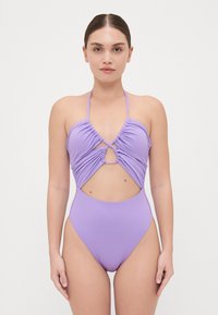 Maillot de bain une pièce violet avec une texture froncée, décolleté plongeant et découpe en trou de serrure au centre. Fines bretelles et jambes échancrées.