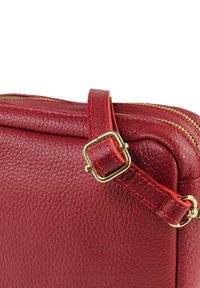 Rote Lederhandtasche mit strukturierter Oberfläche, ausgestattet mit einem goldenen Reißverschluss und einer quadratischen Metall-Schnalle am Riemen, die handwerkliche Details betont.