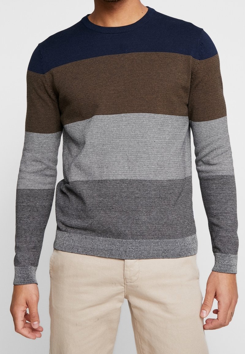 Neulottu villapaita, jossa on vaakasuorat raidat tummansinisestä, ruskeasta, harmaasta ja vaaleasta harmaasta. Pyöreä kaula-aukko, pitkät hihat sekä ribbattu helma ja hihansuut.