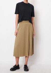 Haut noir à rayures, à manches courtes, associé à une jupe midi plissée beige. L'ensemble se compose d'une taille ajustée et de chaussures noires épaisses.