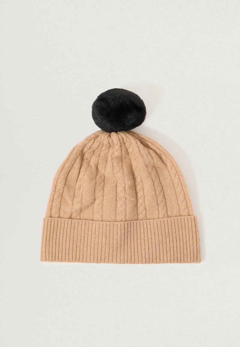 Knit beanie in beige with a ribbed cuff, featuring a textured cable design and a black pom-pom on top. Soft fabric with a cozy appearance.