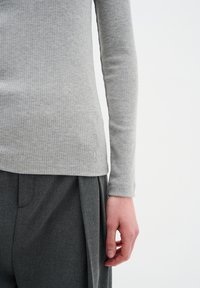 Grå ribbade långärmade toppar i kombination med mörkgrå plisserade byxor. Toppens nederkant har en diskret logotyp. Slät, strukturerad tyg.