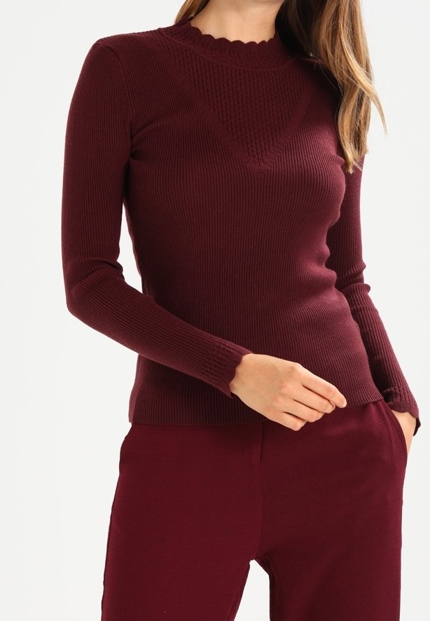 Bordeauxrotes, geripptes Stricktop mit wellenförmigem Ausschnitt, strukturiertem Muster auf der Brust und langen Ärmeln. Eng anliegendes Design mit weichem Stoff.