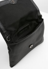 Černá kabelka vyrobená z kombinace kožených a textilních materiálů, s magnetickým zapínáním a vnitřní kapsou na zip.