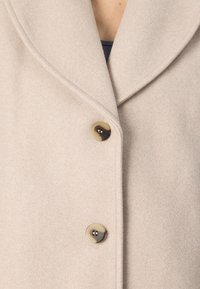 Beige wool blend coat with a shawl collar, featuring two round buttons and a soft, textured surface.