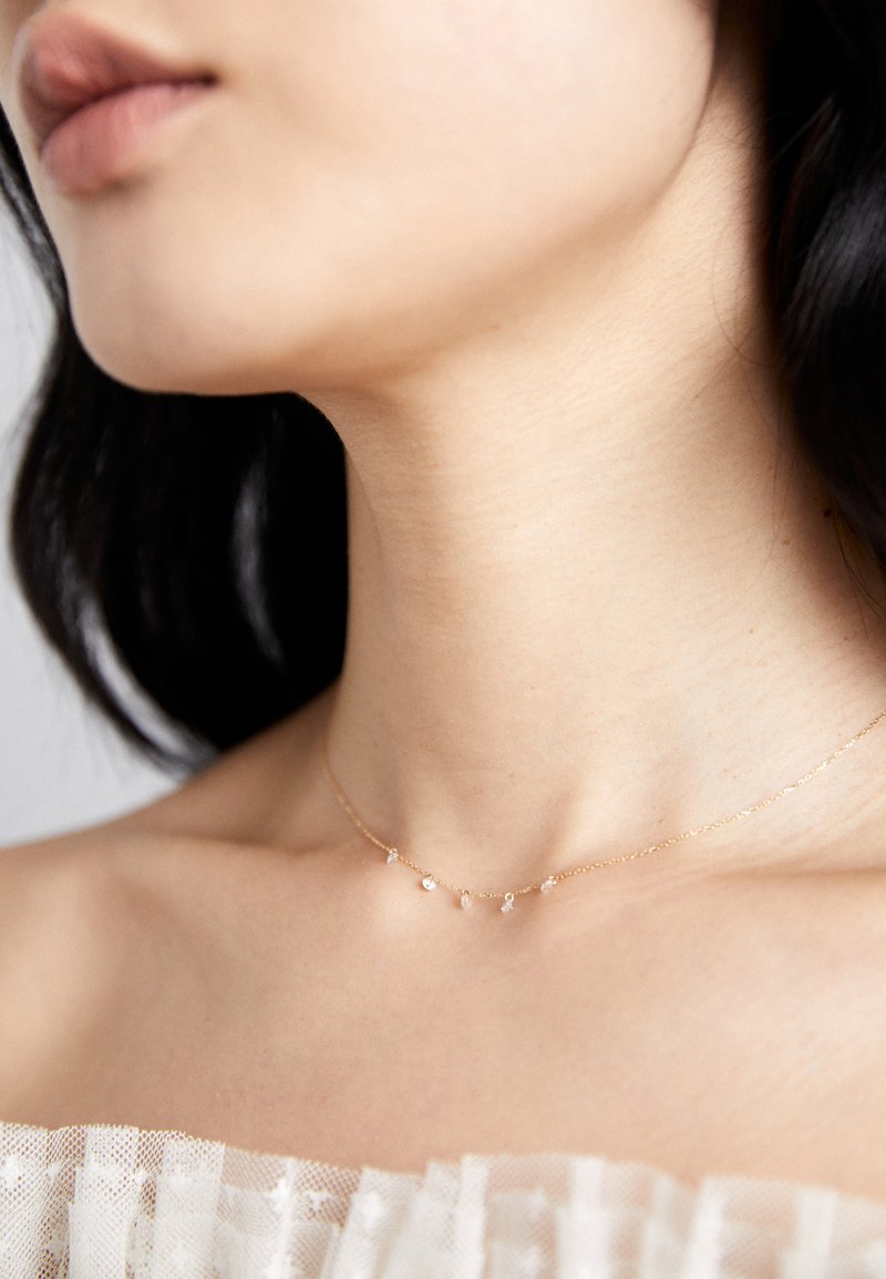 Collar de oro con cinco pequeños y brillantes acentos a lo largo de una delicada cadena, llevado sobre piel desnuda contra un fondo de tela clara.