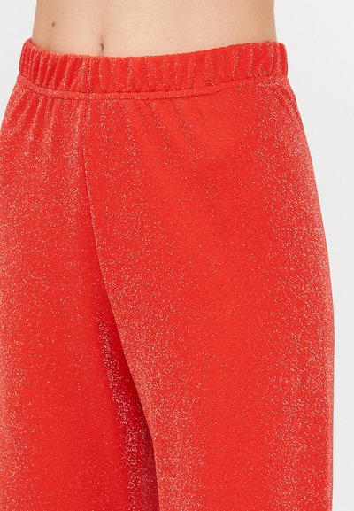 Red jogger pants with a subtle glittery texture, featuring an elastic waistband and smooth material, shown from the waist to mid-thigh.