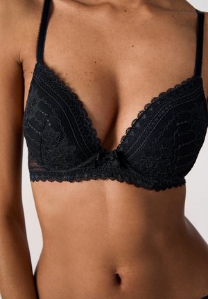Black lace bralette with a deep plunging neckline, scalloped edges, and a satin bow accent in the center, featuring delicate floral patterns.