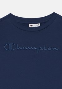 Μπλε σκούρο μπλουζάκι με κοντά μανίκια από βαμβάκι, με κεντημένο λογότυπο "Champion" σε λίγο πιο σκούρα απόχρωση μπλε στο μπροστινό μέρος.