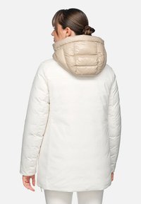 Giacca a vento bianca con cappuccio trapuntato beige. Presenta una linea dritta e dettagli minimi. Tessuto liscio con una finitura elegante.