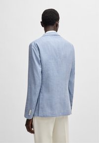 Blå linneblazer med en texturerad yta, enkel slits och detaljer med fyra knappar vid ärmsluten. Designen har en klassisk krage.