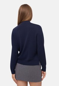 Maglione lavorato a maglia blu navy con scollatura rotonda, maniche lunghe, polsini e orlo a coste. Abbinato a una mini gonna grigia a quadri.
