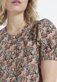 Floral blouse featuring a round neckline, short puff sleeves, and button closure. Pattern includes orange, green, and black floral motifs.