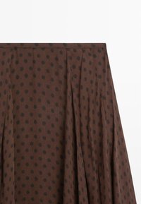 Tissu marron à pois noirs, avec des plis verticaux et une ceinture, probablement une partie d'une jupe ou d'un vêtement.